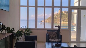 Salón con un amplio ventanal que ofrece vistas al mar, incluyendo un faro y un barco.