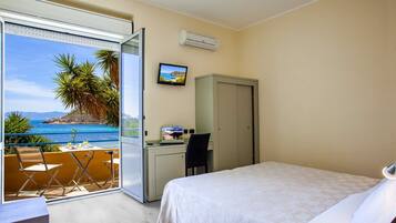 Une chambre d’hôtel avec un lit, un bureau équipé d’un ordinateur, une chaise et une vue sur la mer, accessible par une porte coulissante.