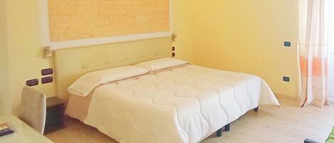 Un dormitorio ordenado con cama, mesitas de noche y una lámpara fijada a la pared.