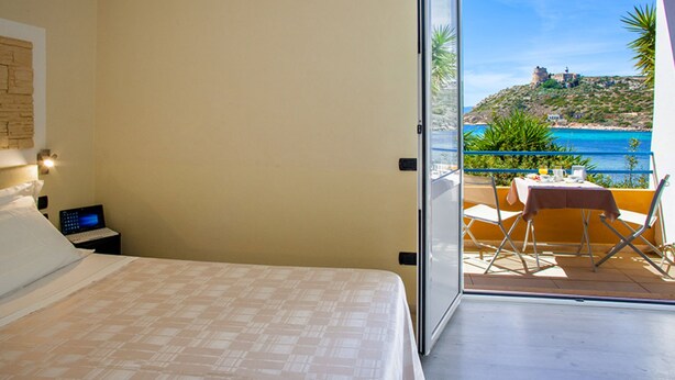 A bedroom with a bed, a laptop on a nightstand, and a balcony with a table and chairs.