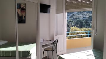 Ein Schlafzimmer mit einem Bett, einem Schreibtisch und einem Sessel. An der Wand ist ein Fernseher angebracht.