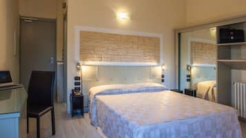 A hotel room with a bed, a desk with a laptop, a chair, a nightstand, a mirror, and a wardrobe.