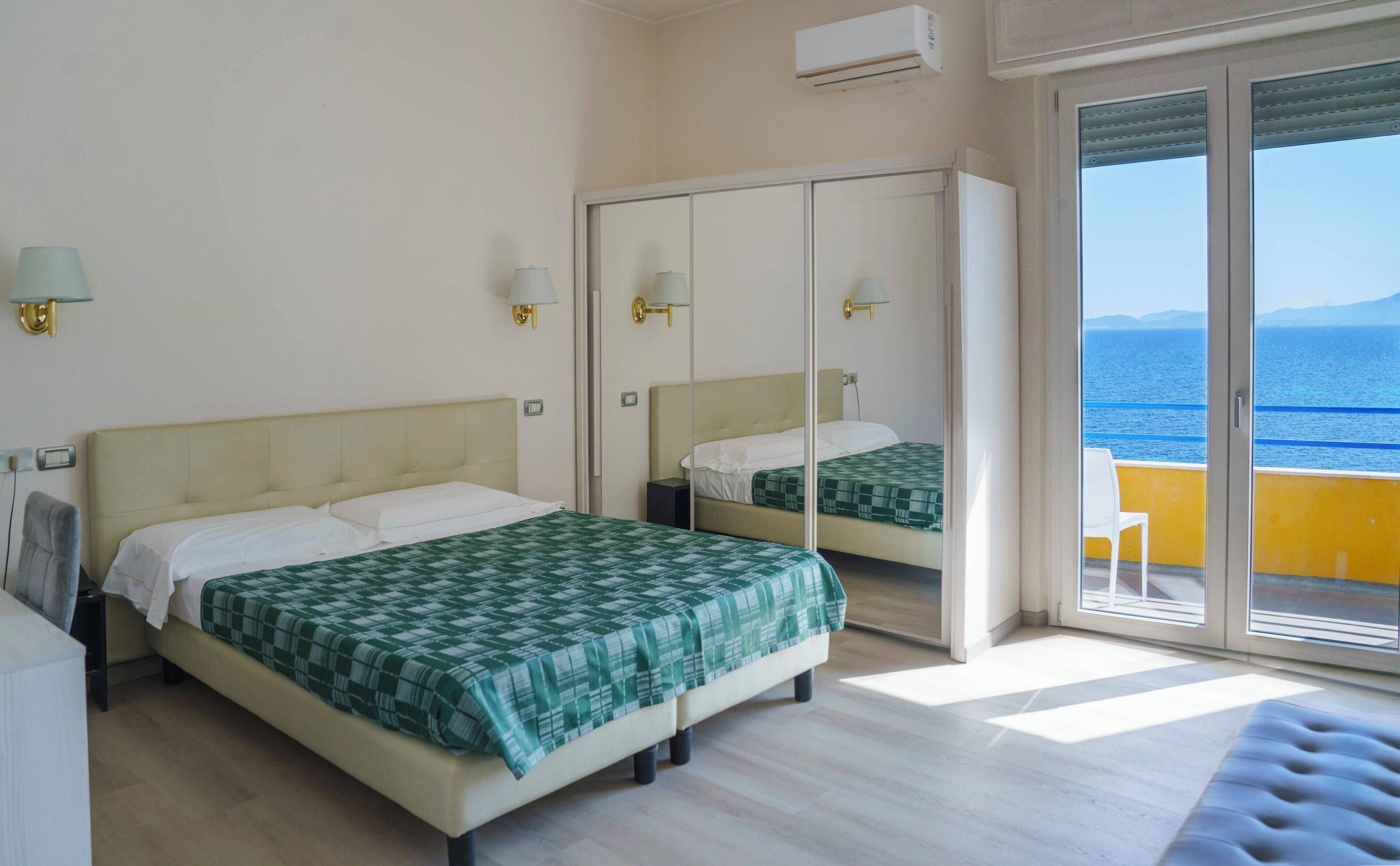 A hotel room with two beds, a balcony with a view of the sea, and an air conditioning unit.