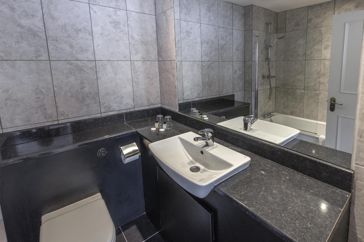 A modern bathroom with a black countertop, two sinks, a toilet, and a shower.