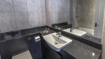 Un baño moderno con encimera negra, dos lavamanos, inodoro y ducha.