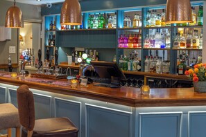 A bar area with a counter, bar stools, and shelves stocked with various bottles. - Kings Court Hotel, BW Signature Collection (Alcester)