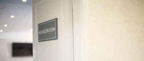 A door labeled "BOARDROOM" with a plain wall and ceiling lights in the background.