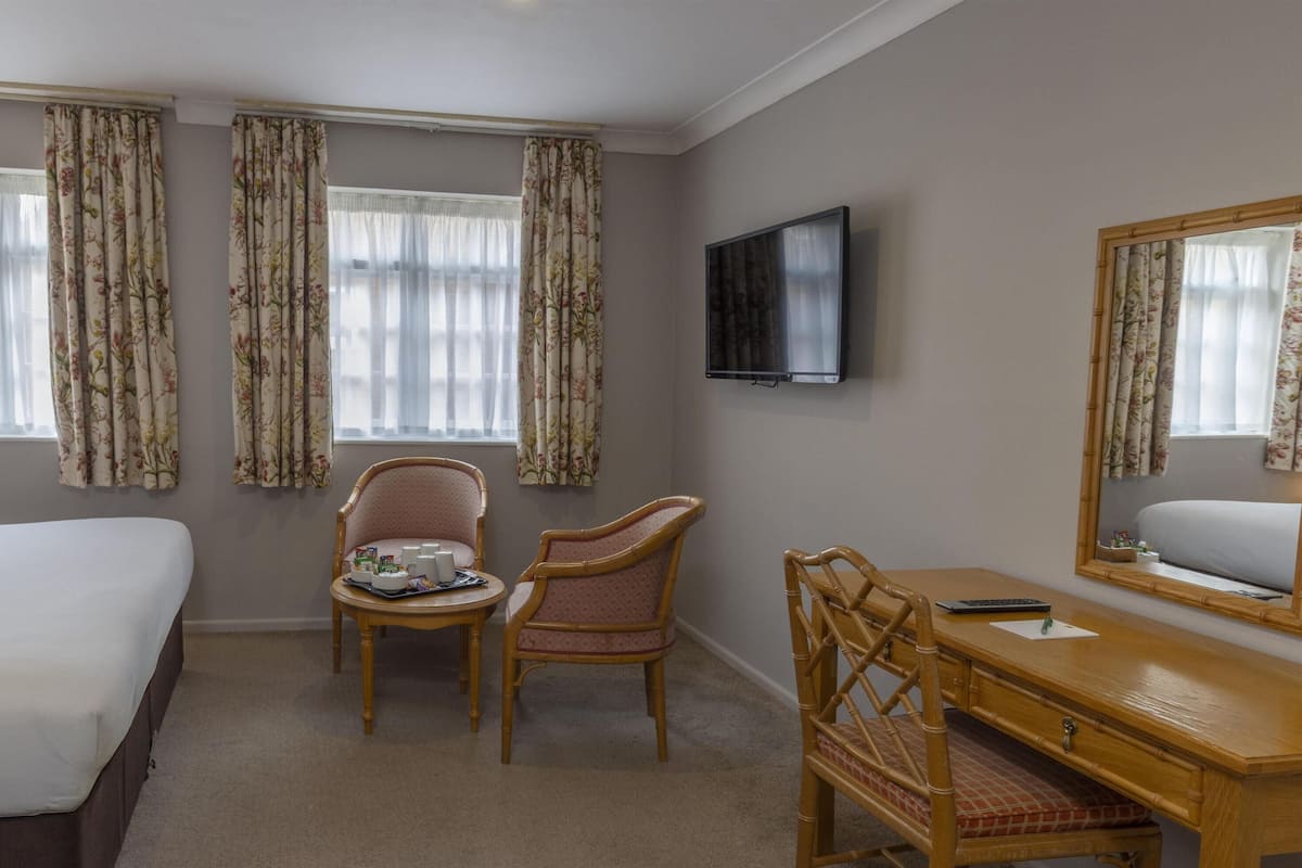 A hotel room with a bed, two chairs, a desk, a television, and a mirror.