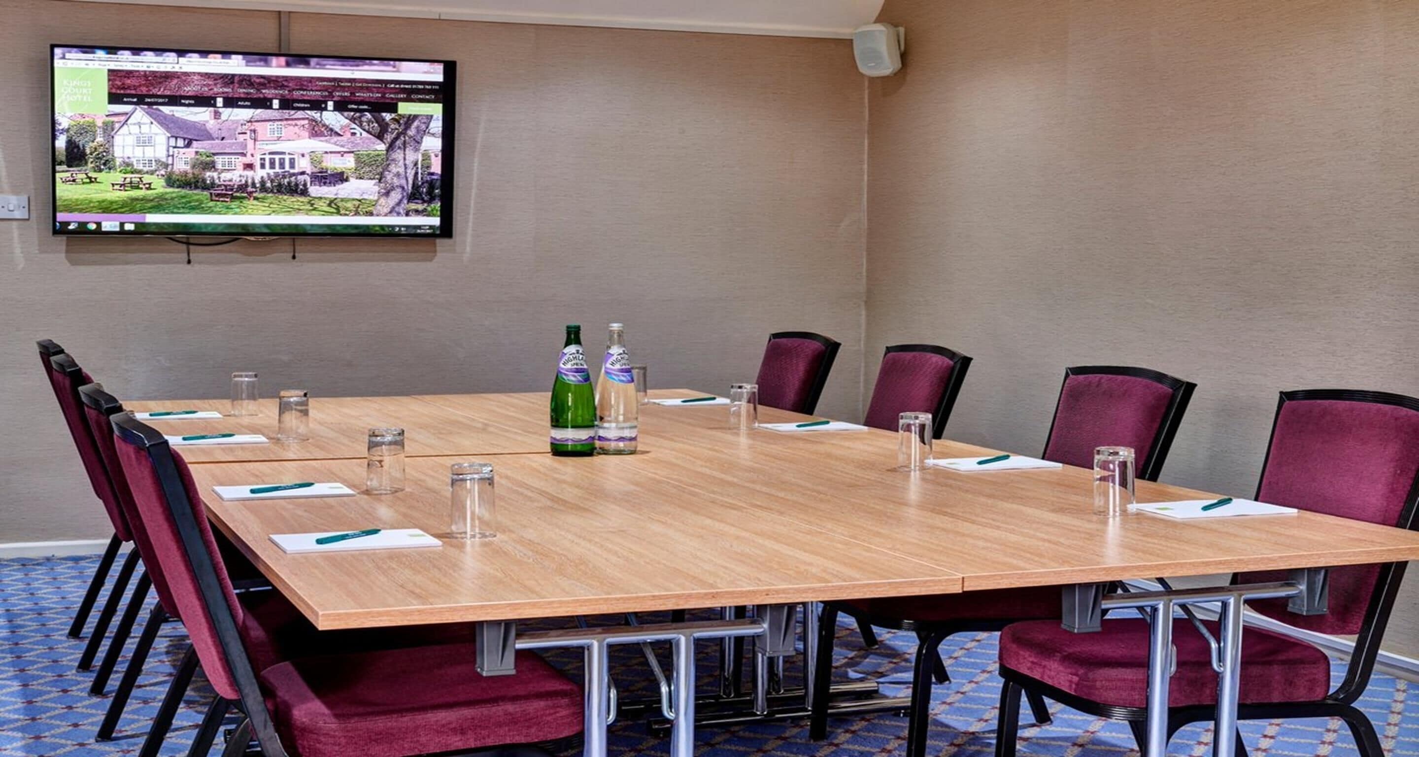 A conference room with a long table, red chairs, and a television on the wall.