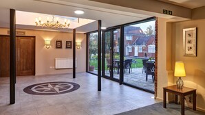 A hotel lobby with a large glass door leading to an outdoor patio, a chandelier, a framed picture on the wall, and a small table with a lamp. - Kings Court Hotel, BW Signature Collection (Alcester)