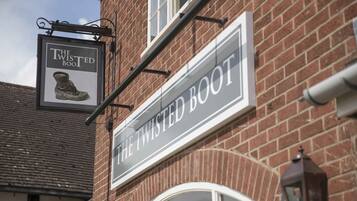 Une enseigne pour le pub « The Twisted Boot », avec une illustration de botte et la façade classique d’un bâtiment en briques.