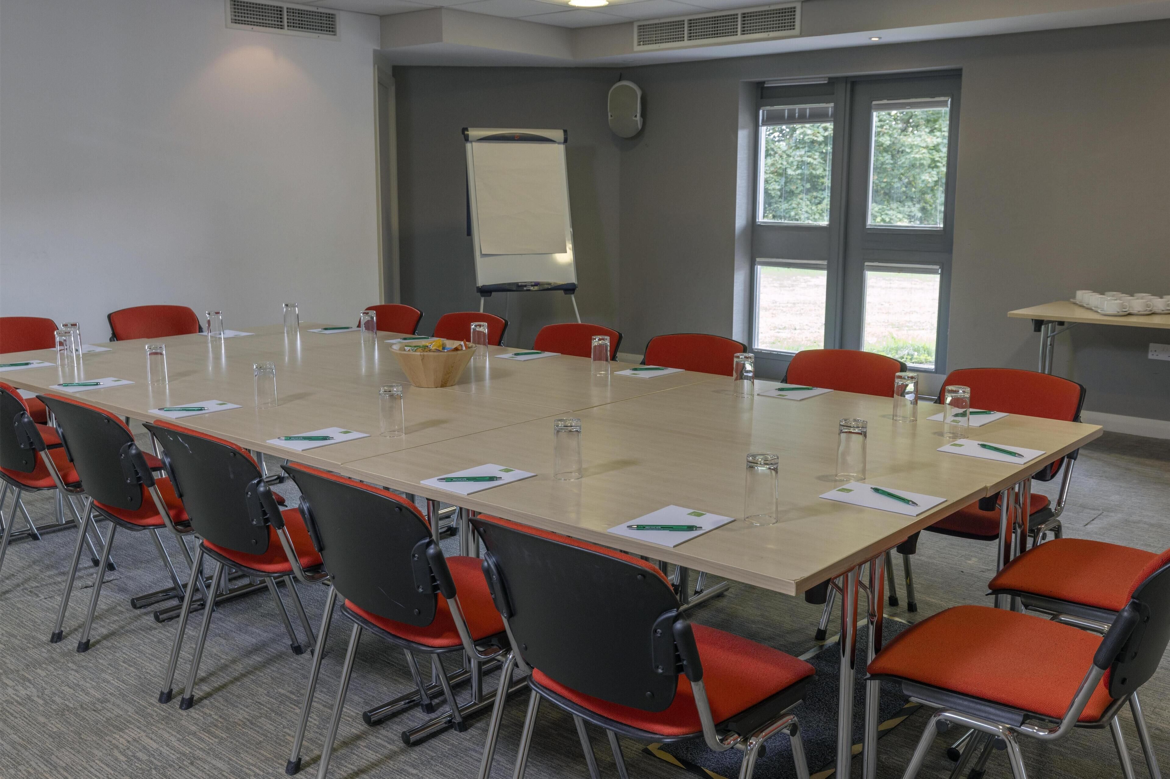 A conference room with a long table, red chairs, and a whiteboard.