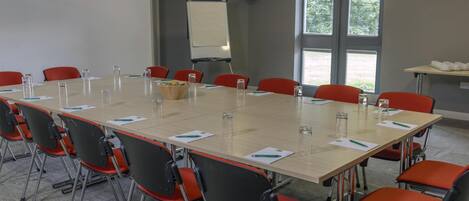 A conference room with a long table, red chairs, and a whiteboard.