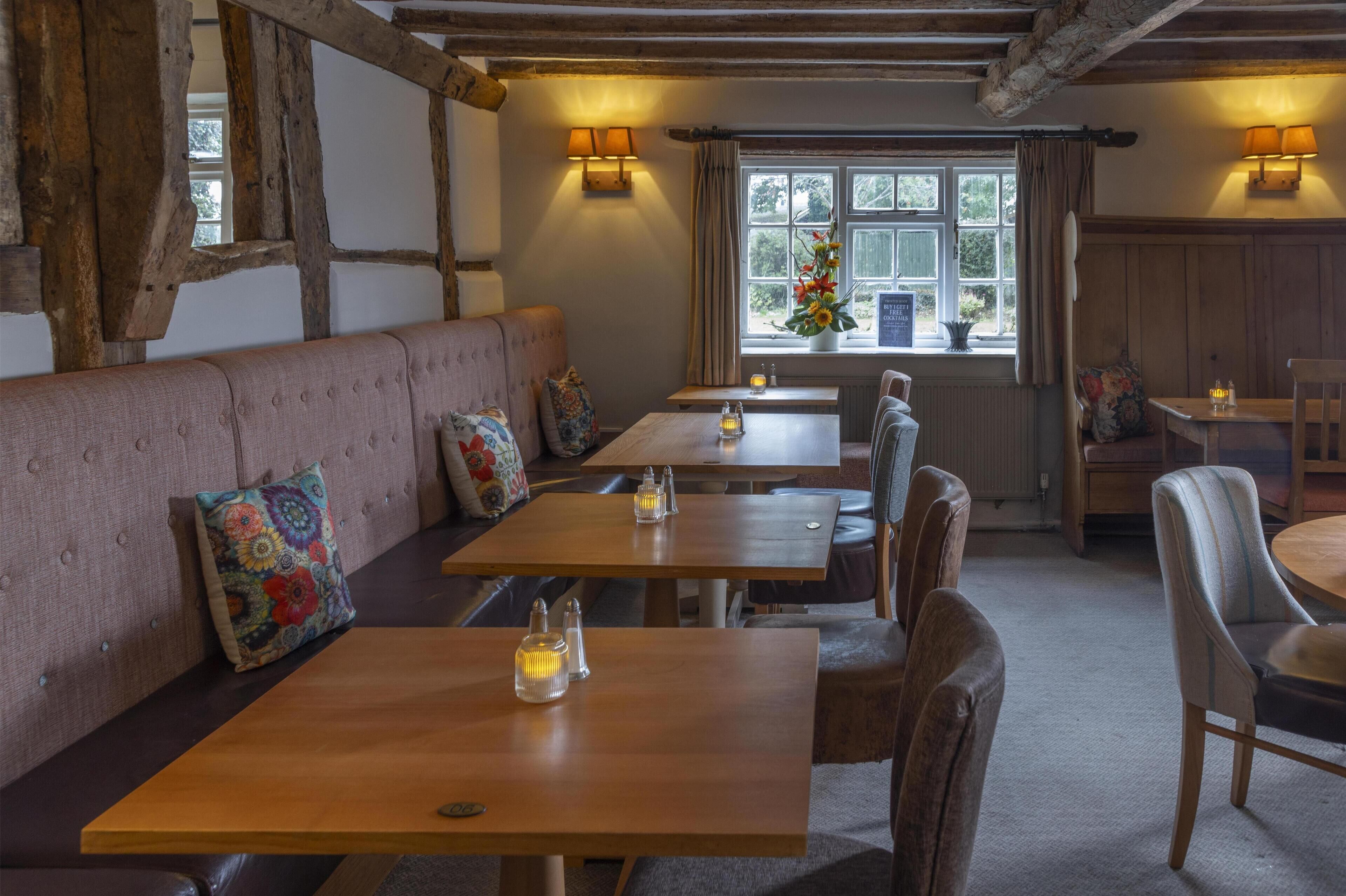 A cozy restaurant with wooden tables and benches, warm lighting, and a view of the outdoors through large windows.