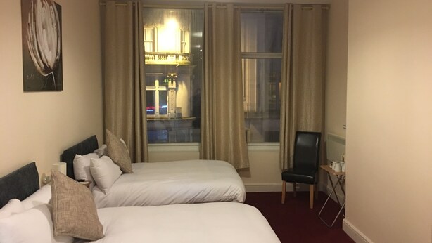 Une chambre d’hôtel avec deux lits, une chaise, une lampe et une fenêtre avec des rideaux.