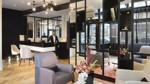 A modern hotel lobby with a reception desk, seating area, and large windows. - Hotel Le Relais du Marais (Paris)