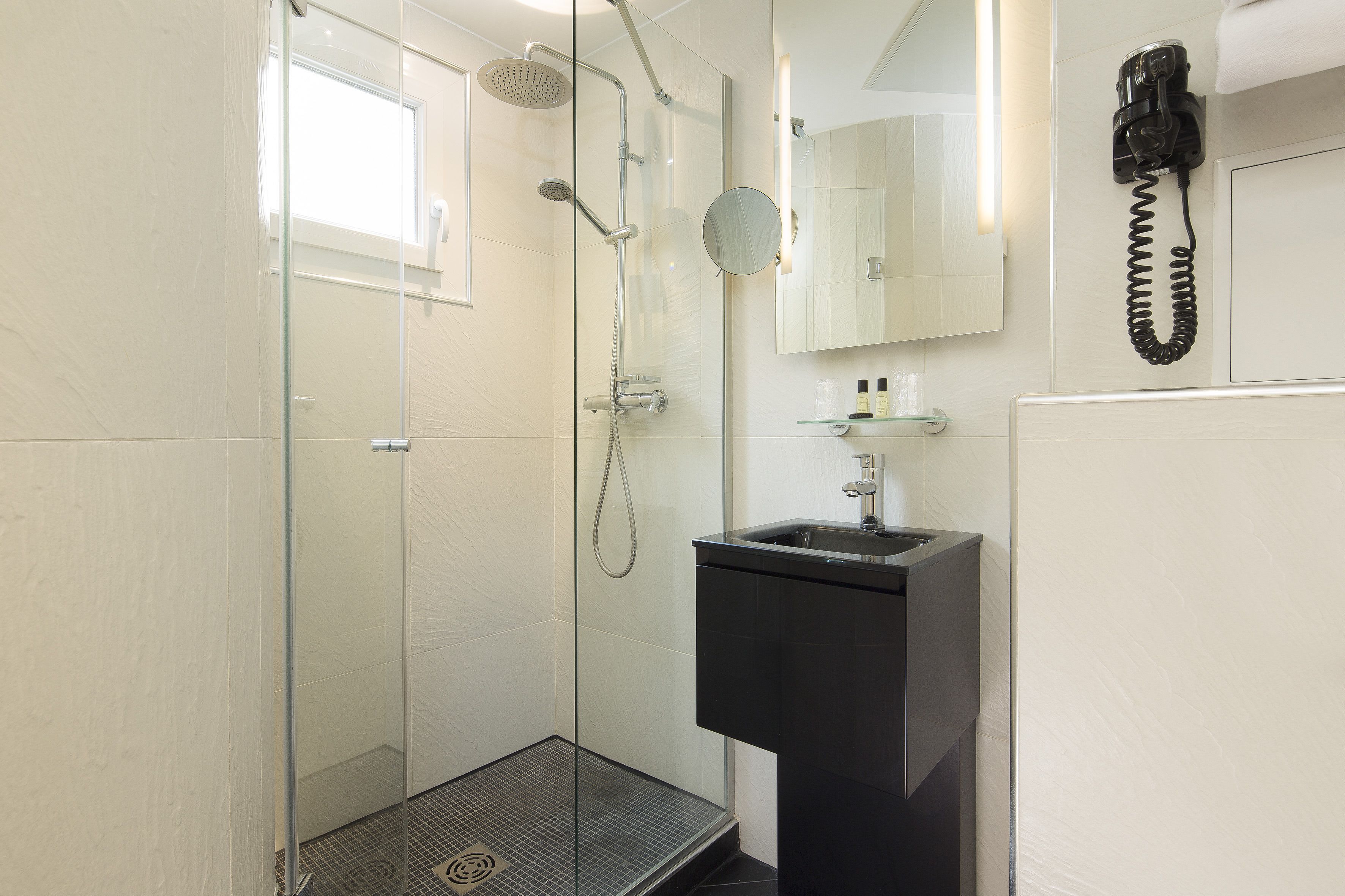 A modern bathroom with a glass-enclosed shower, a black sink, and a mounted telephone.