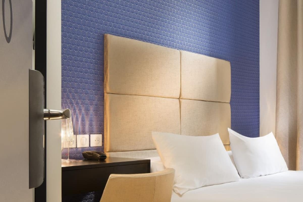 A hotel room with a large bed, a headboard, a nightstand, a chair, and a window with curtains.
