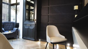 A modern interior with a dark wall, a light-colored armchair, a blue sofa, and a small table with a lamp. - Hotel Le Relais du Marais (Paris)