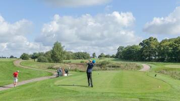 A golf course with a clear sky, a golfer in mid-swing, and a path leading to a tee box.