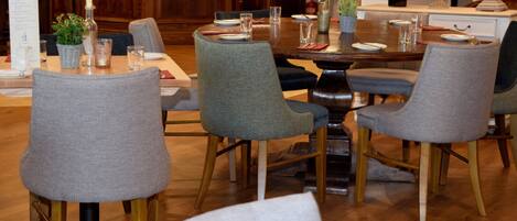 A dining area with a wooden table, grey upholstered chairs, and a bar in the background.