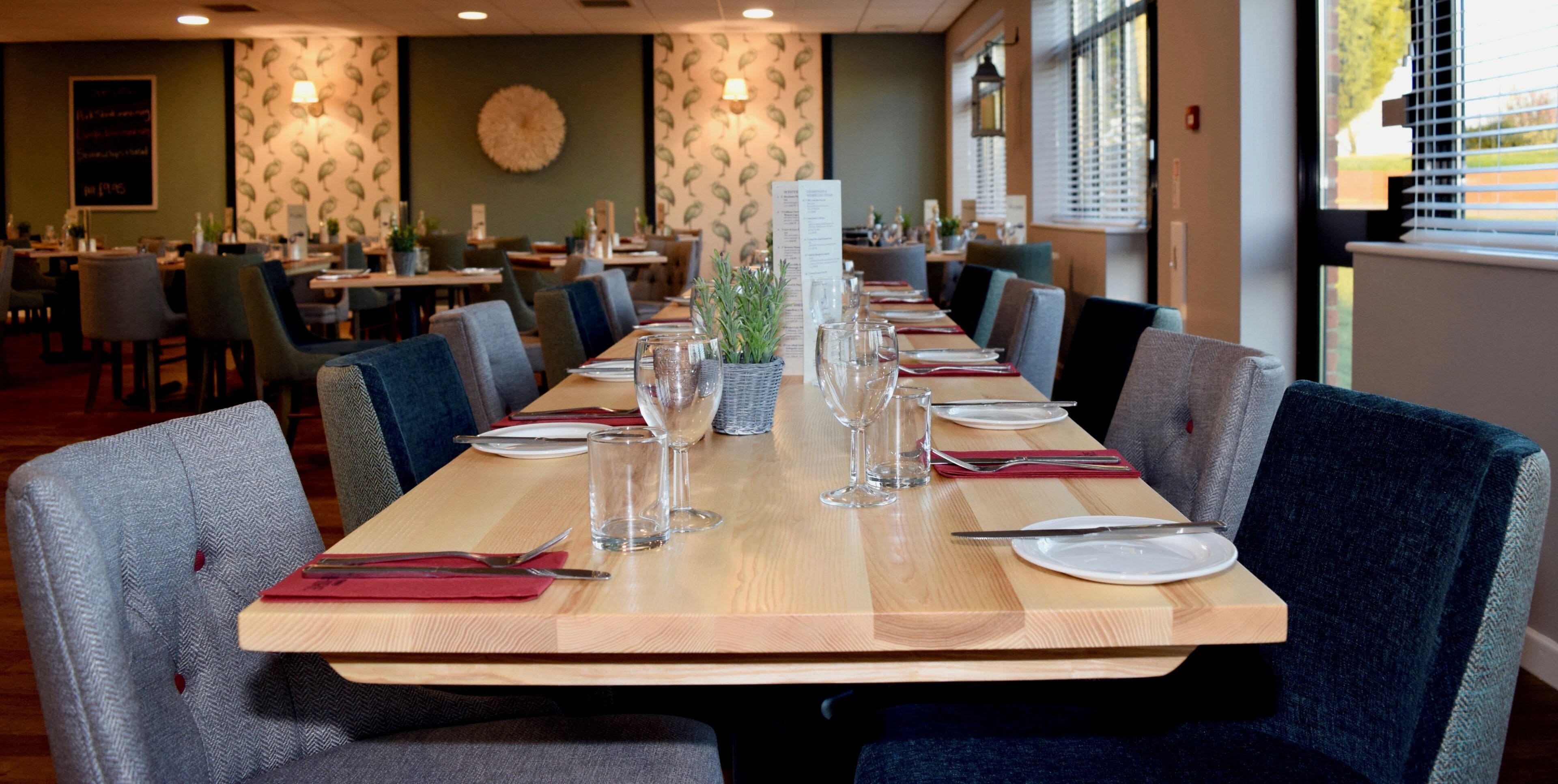 A restaurant with a long wooden table set for dining, surrounded by chairs.