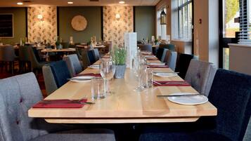 A restaurant with a long wooden table set for dining, surrounded by chairs.