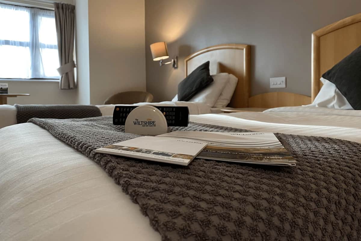 A hotel room with a bed, a remote control, a magazine, and a lamp.