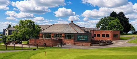 A golf club with a brick building, a well-maintained lawn, and a clear sky.
