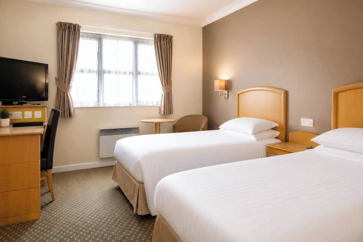 A hotel room with two beds, a desk, a chair, a television, and a window with curtains.