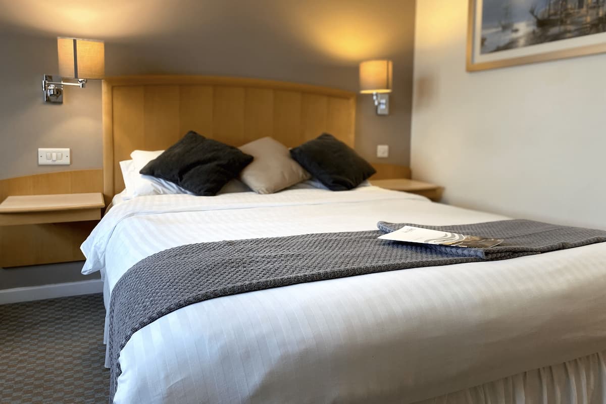A hotel room with a bed, two bedside lamps, a nightstand, a framed picture on the wall, and a power outlet.