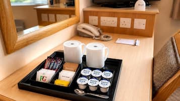 A hotel room with a wooden desk, a tray with breakfast items, a telephone, a TV, and a mirror.