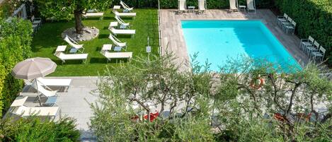A swimming pool surrounded by lounge chairs and a tree, with a hedge in the background.