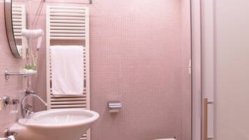 Un baño con lavamanos, dos inodoros, un perchero, un espejo y una toalla colgada en la pared.