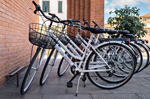 Una fila di biciclette con cestini, recanti il marchio "HOTEL SAN MARCO", parcheggiate contro un muro di mattoni.