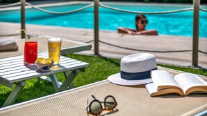 A poolside setting with a table holding a drink, a bowl of chips, a hat, and an open book. - Hotel San Marco (Lucca)