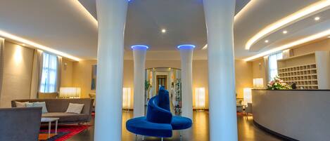 En moderne lobby med en blå sofa, hvide søjler og en receptionsdisk.