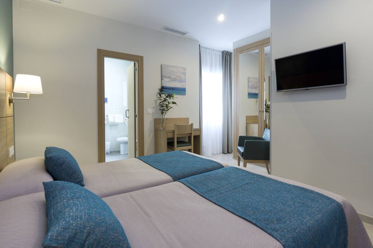 Habitación de hotel con cama, escritorio, silla, televisión y baño visible a través de una puerta abierta.