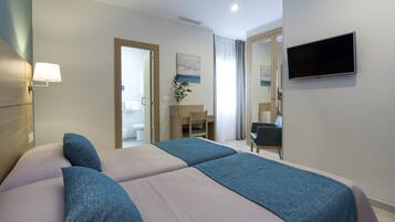 Une chambre d’hôtel avec un lit, un bureau, une chaise, une télévision et une salle de bain visible à travers une porte ouverte.