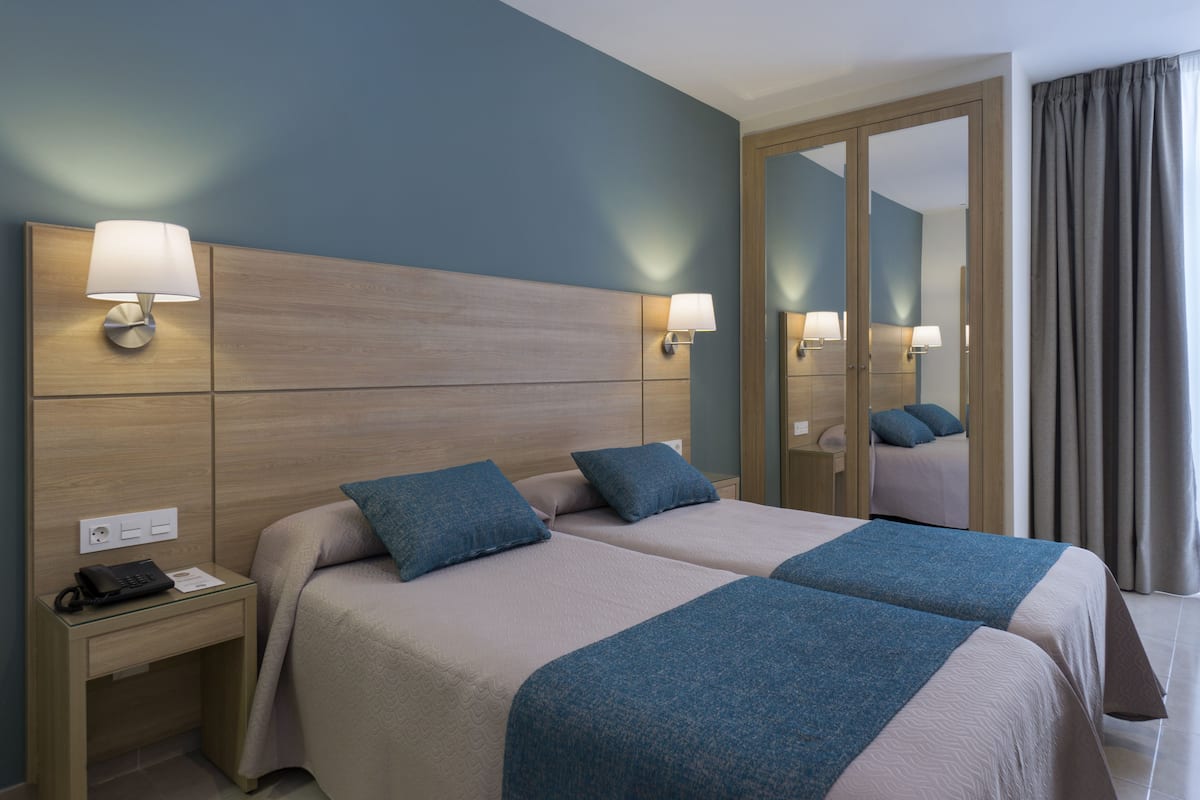 Habitación de hotel con dos camas, una mesita de noche, un espejo y vistas al exterior.