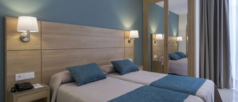 A hotel room with two beds, a nightstand, a mirror, and a view of the outside.