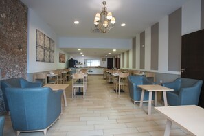 A spacious dining area with wooden tables and blue upholstered chairs, a chandelier, and artwork on the walls. - Hotel Sur Málaga (Málaga)