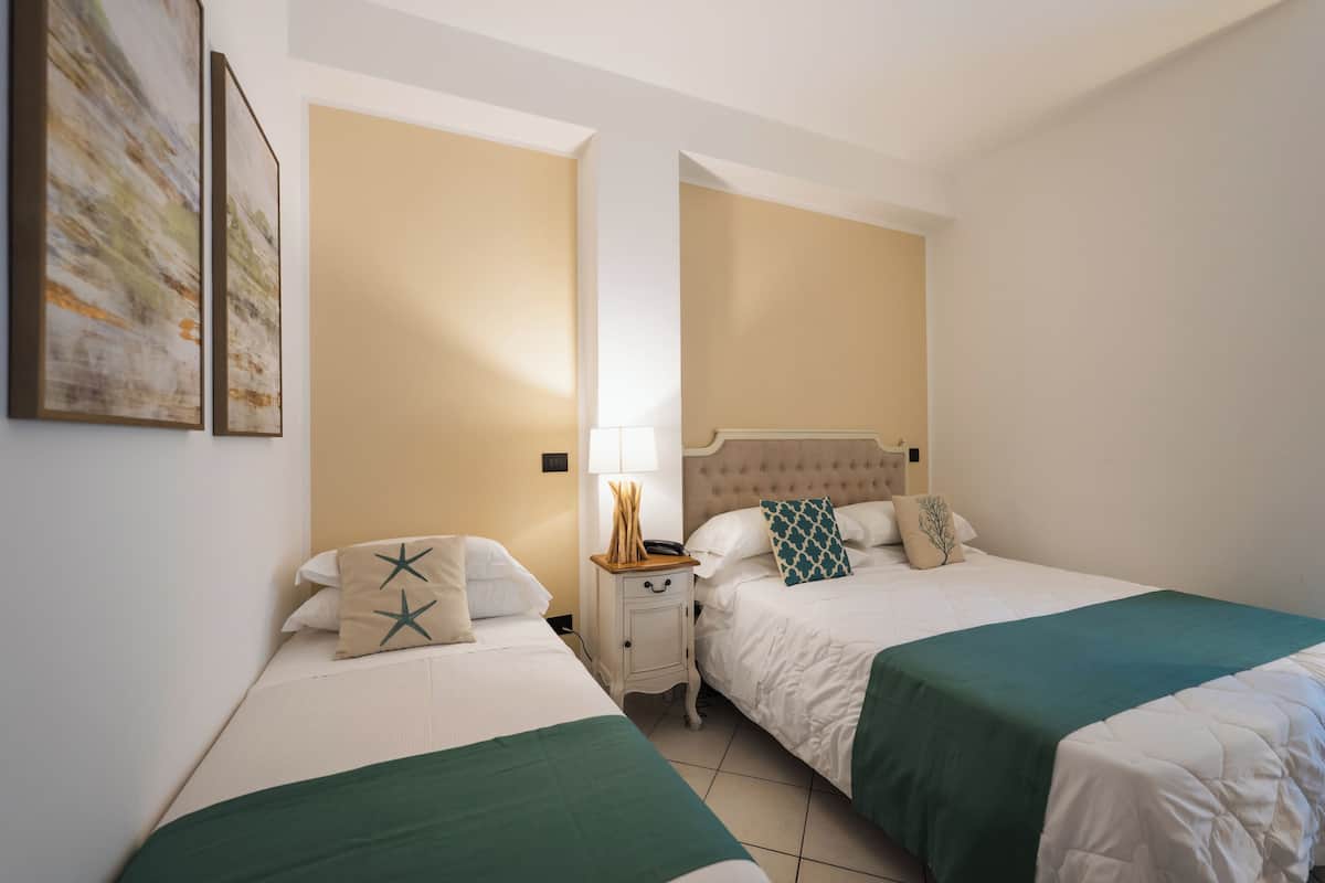 A hotel room with two beds, a nightstand, a lamp, and a wall-mounted artwork.