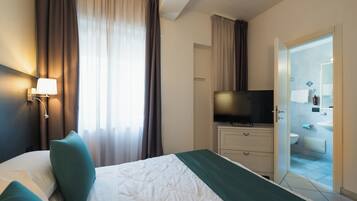 Une chambre d’hôtel avec un lit, une télévision, une salle de bain visible à travers une porte ouverte et une fenêtre avec des rideaux.