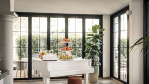 Una mesa blanca con un piano, una exhibición de frutas y una planta en maceta en una habitación con ventanales amplios.