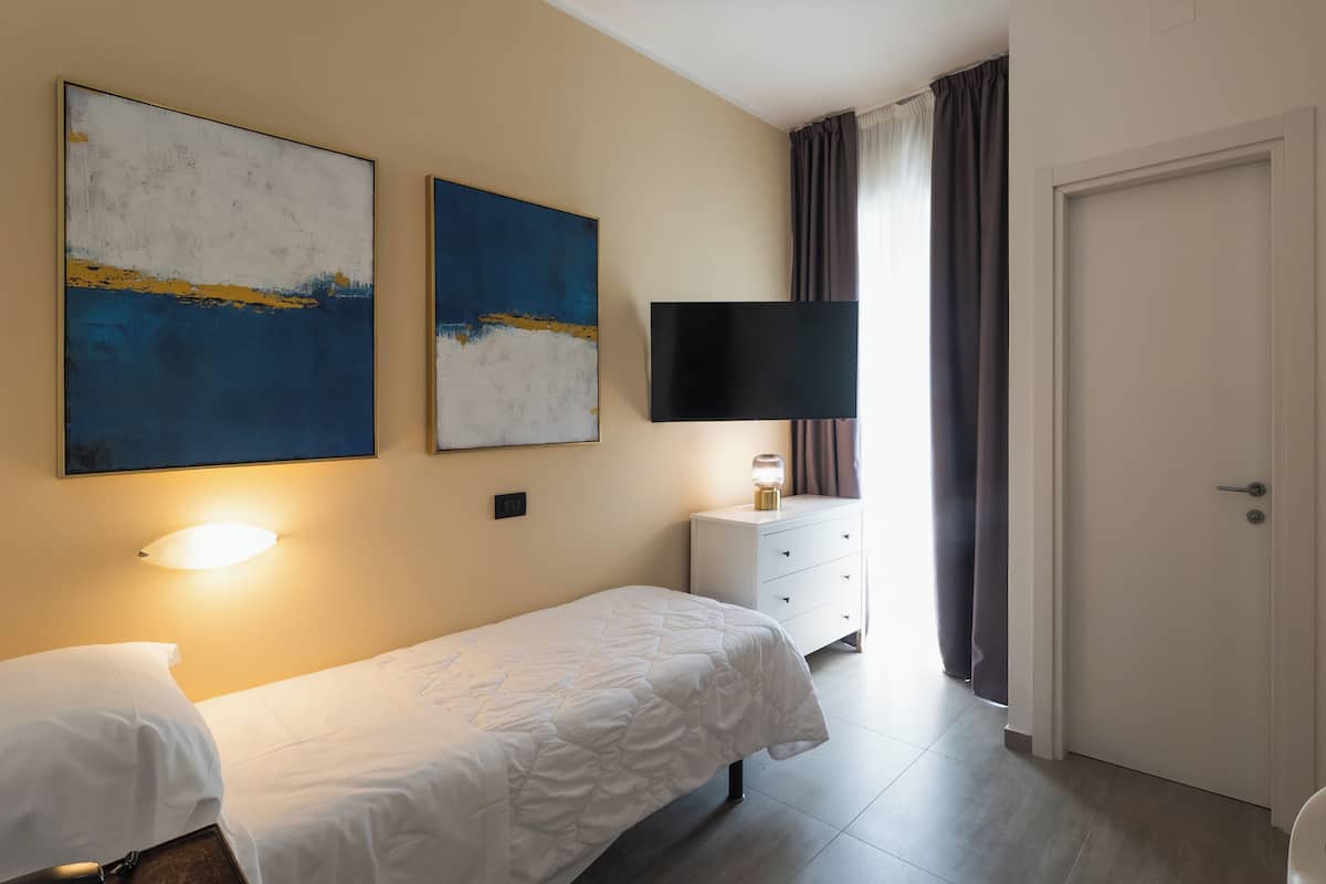 A hotel room with a bed, a TV, a dresser, and two abstract paintings.