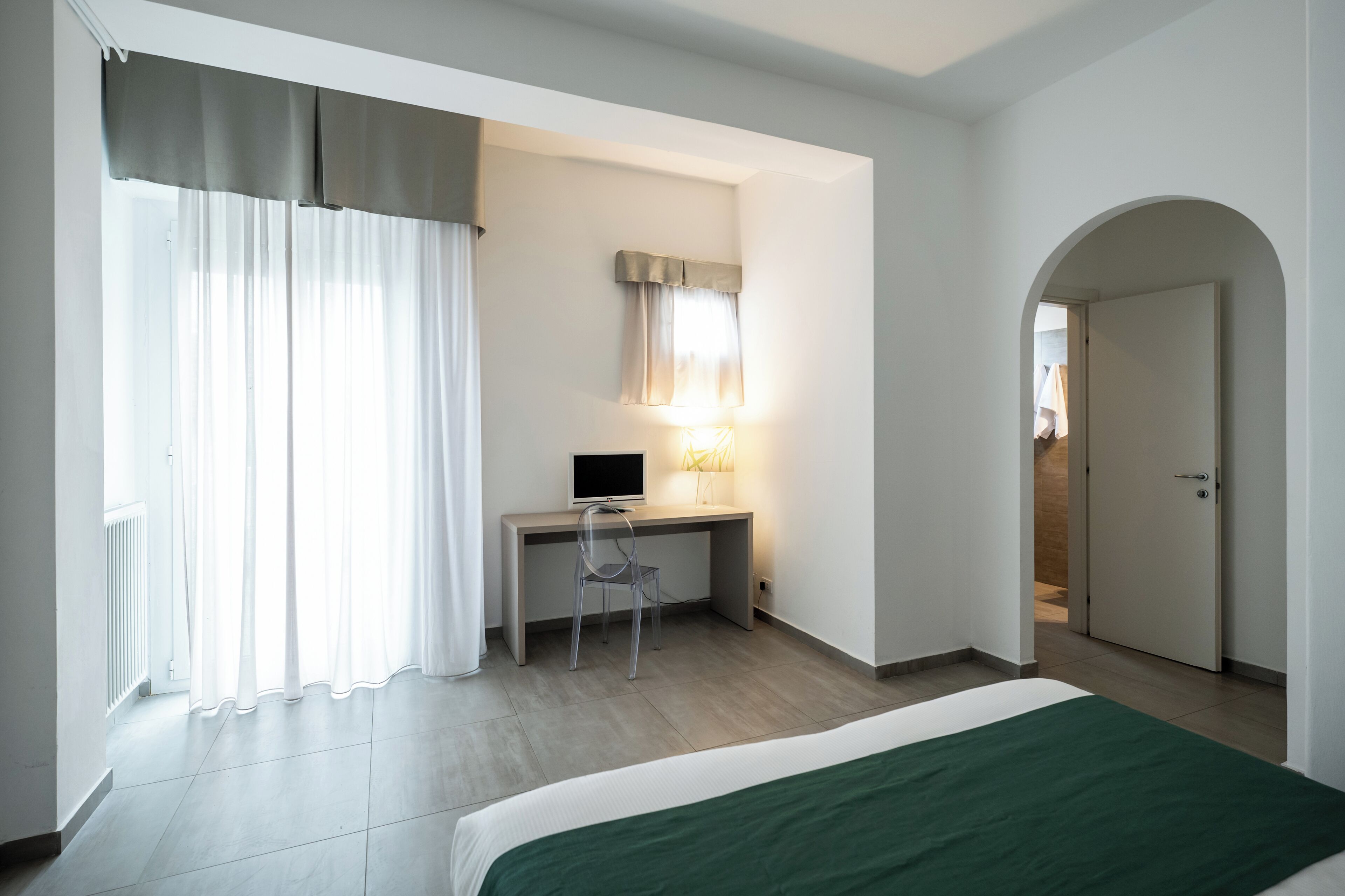 Ein Schlafzimmer mit einem Bett, einem Schreibtisch mit Stuhl, einem Computer und einer Lampe.