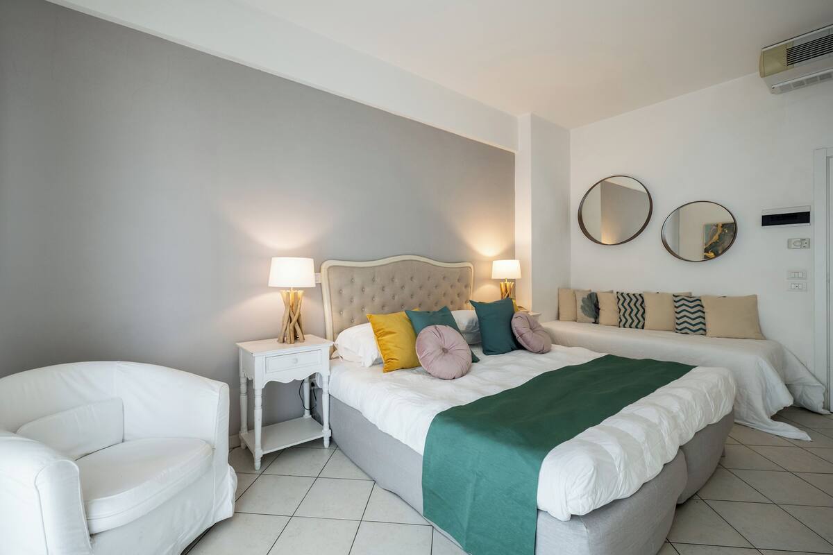 A bedroom with a large bed, two bedside tables, a chair, and two wall-mounted mirrors.
