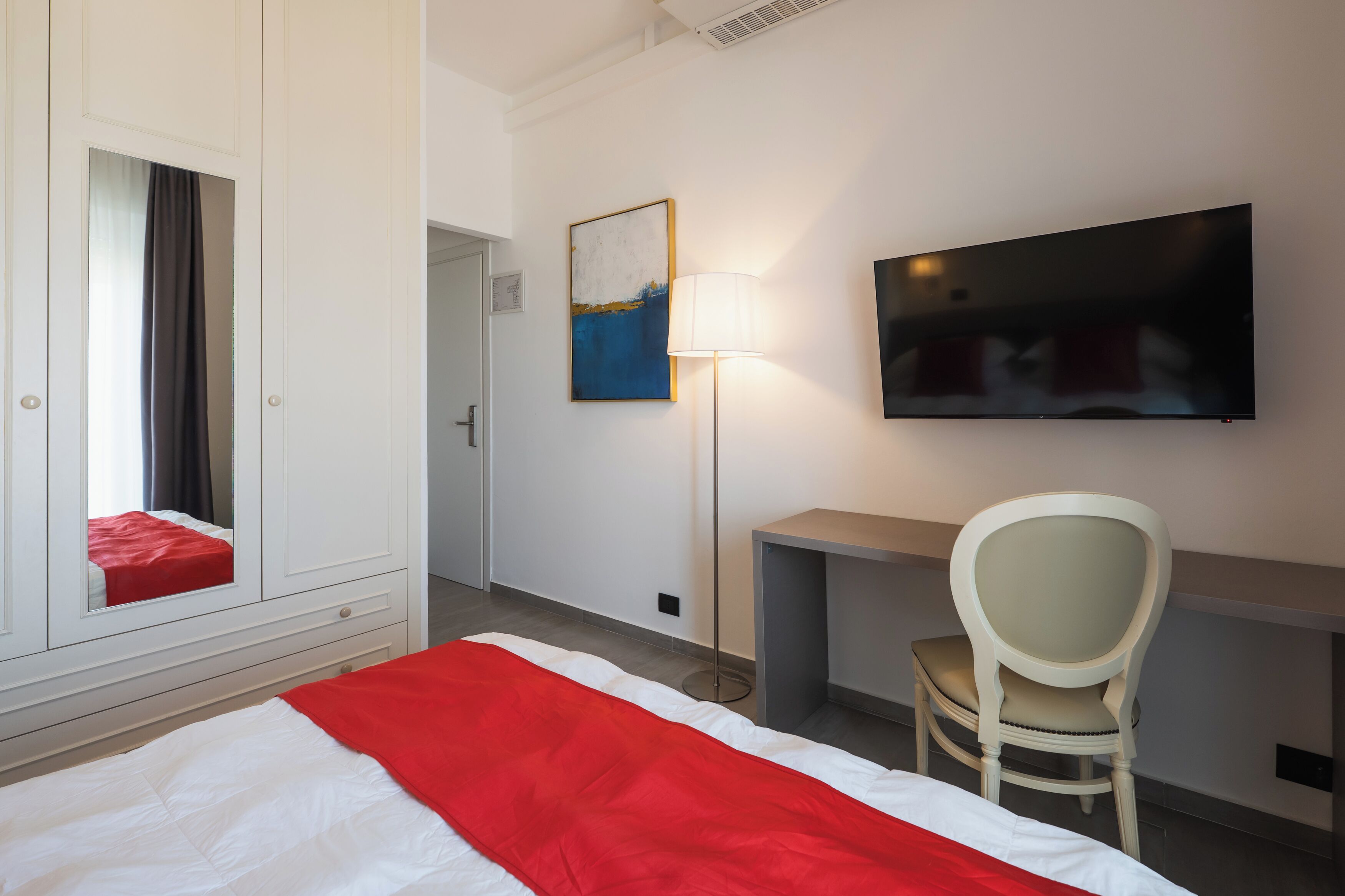 Une chambre d’hôtel avec un lit, un bureau, une chaise, une télévision et un tableau au mur.