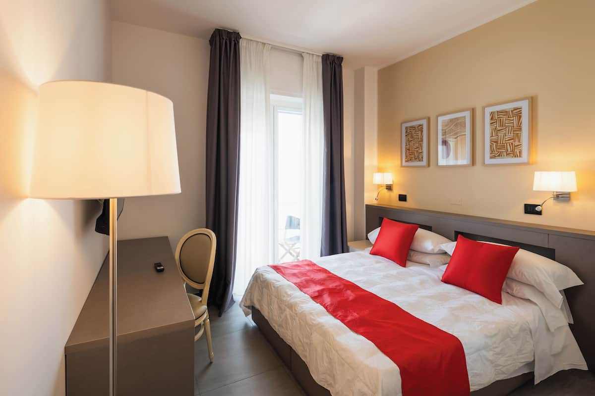 A hotel room with a bed, a desk, a chair, a lamp, and three wall-mounted picture frames.